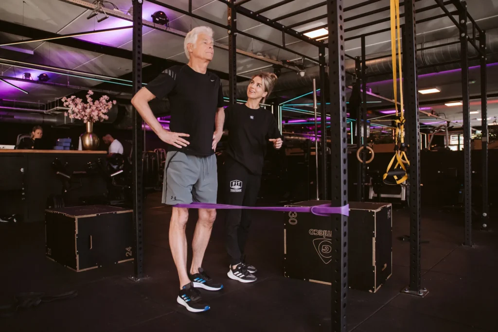 Fysiotherapeut en cliënt bij een balansoefening met weerstandsband in de gym